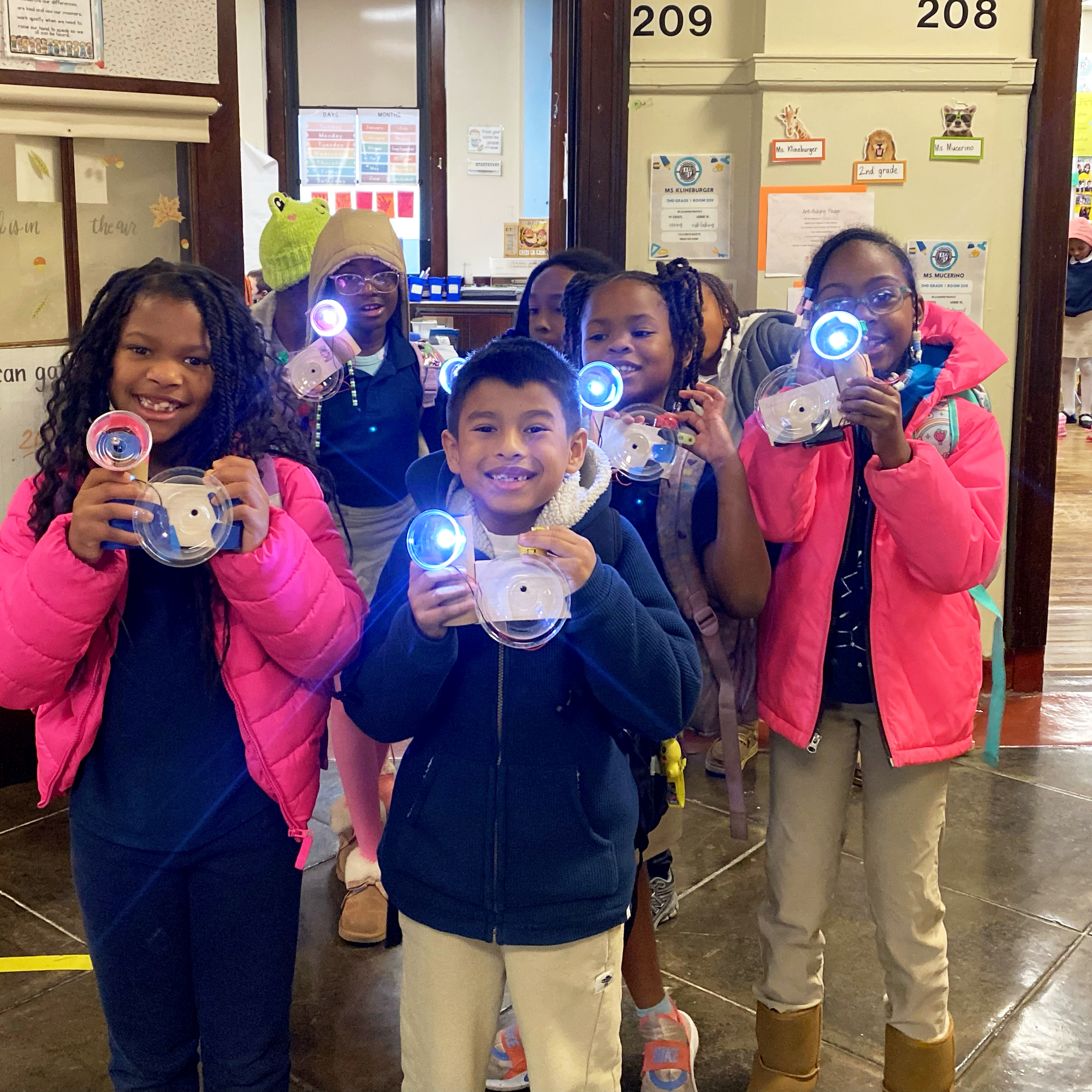 Students Explore Science at John S. Jenks Academy for the Arts & Sciences Students at John S. Jenks Academy for the Arts & Sciences holding illuminated science projects in a school hallway.